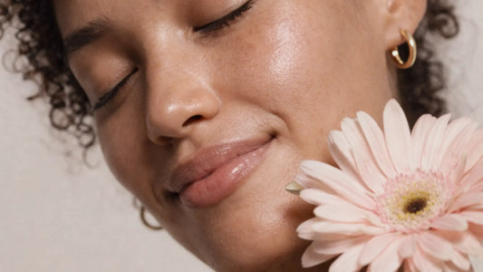 Close-up of a woman with glowing skin holding a pink flower near her face.